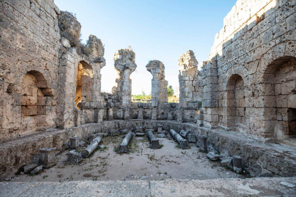 Ancient Roman bath ruins with arched niches and stone columns in Perge, Antalya, Turkey, illuminated by natural light.
