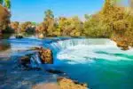 Manavgat Waterfall in Antalya, showing cascading waters surrounded by lush greenery and rocks.