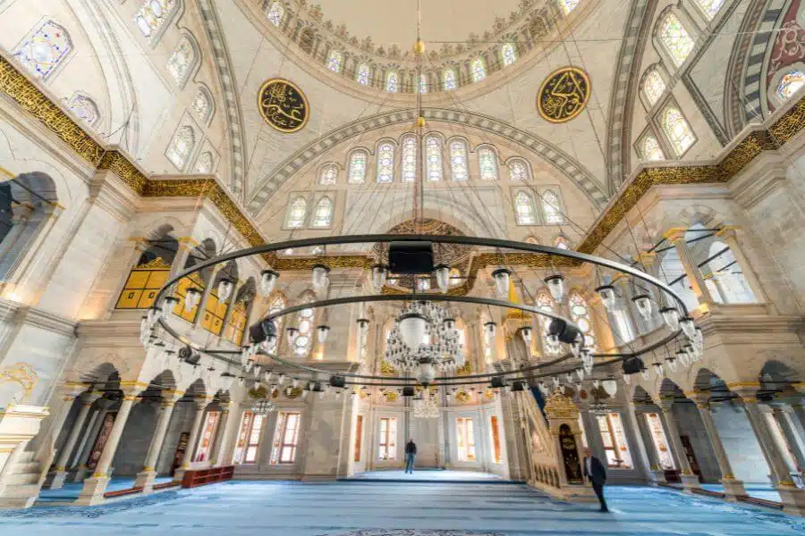 Interior view of the Blue Mosque, showcasing its intricate blue tiles, grand domed ceilings, and elegant chandeliers illuminating the vast prayer hall.